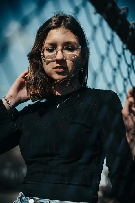 Une femme portant des lunettes touchant un grillage au premier-plan.